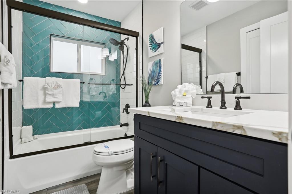 Full bathroom featuring vanity, combined bath / shower with glass door, wood-type flooring, and toilet