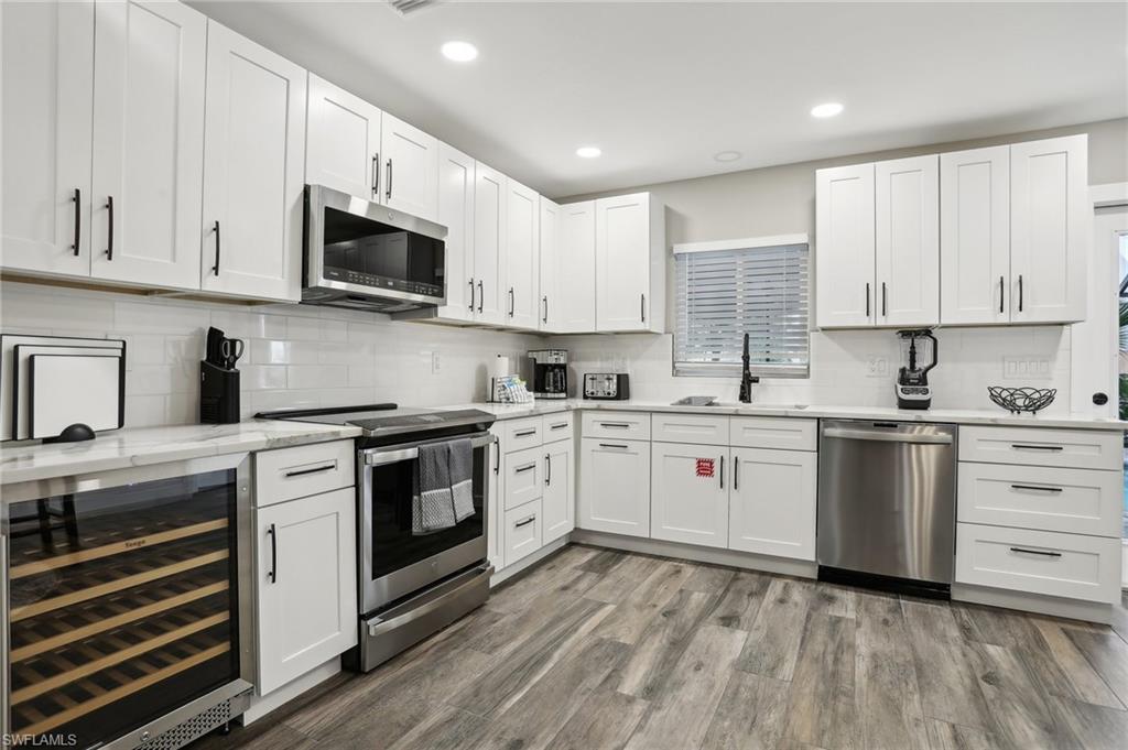 Kitchen with wood-type flooring, stainless steel appliances, decorative backsplash, sink, and wine cooler