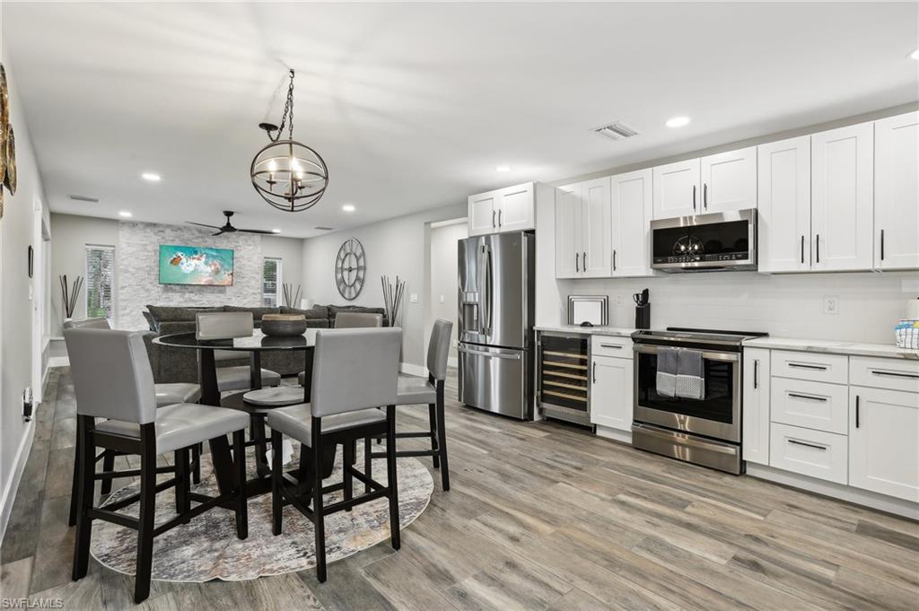 Kitchen with white cabinetry, beverage cooler, light hardwood / wood-style flooring, and appliances with stainless steel finishes