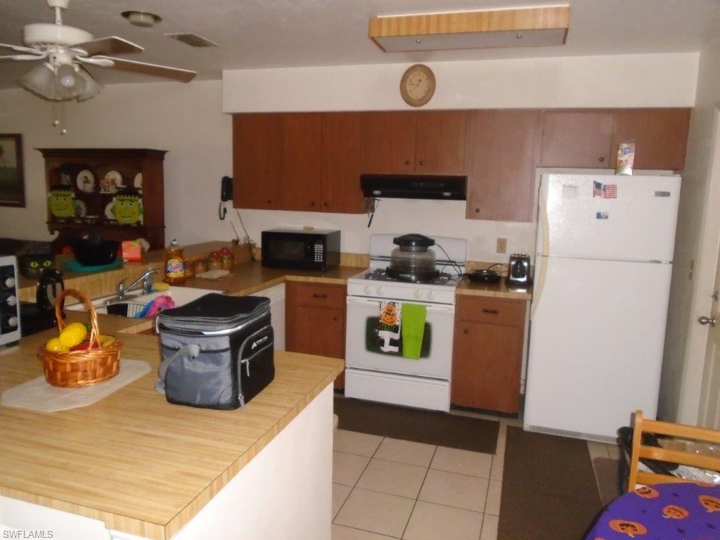 Kitchen featuring ceiling fan, white appliances, sink, exhaust hood, and light tile patterned floors