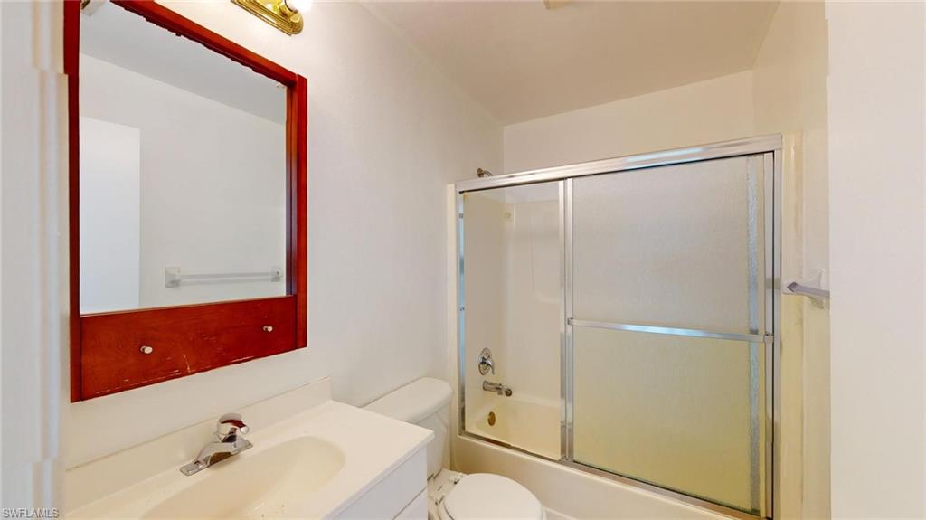 Full bathroom featuring vanity, bath / shower combo with glass door, and toilet