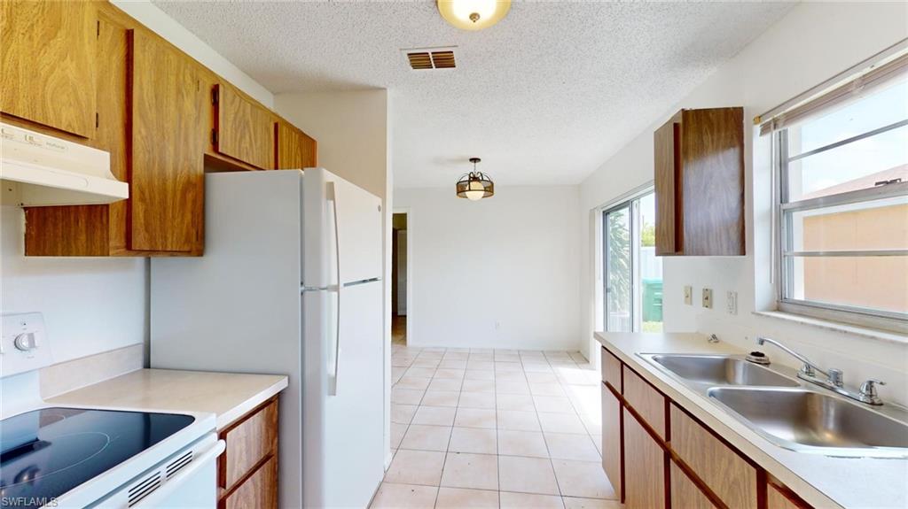 Kitchen with white electric range, light tile patterned floors, sink, and a textured ceiling