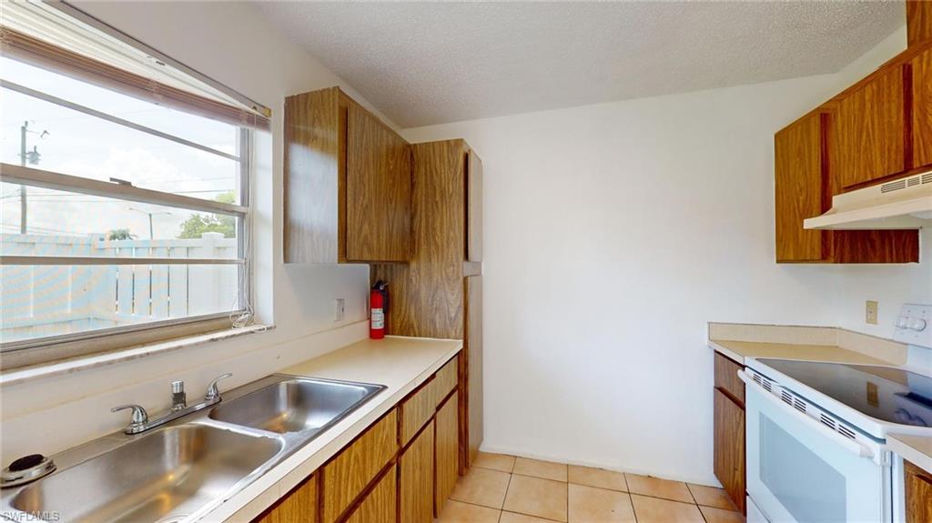 Kitchen with a textured ceiling, sink, light tile patterned floors, and electric stove