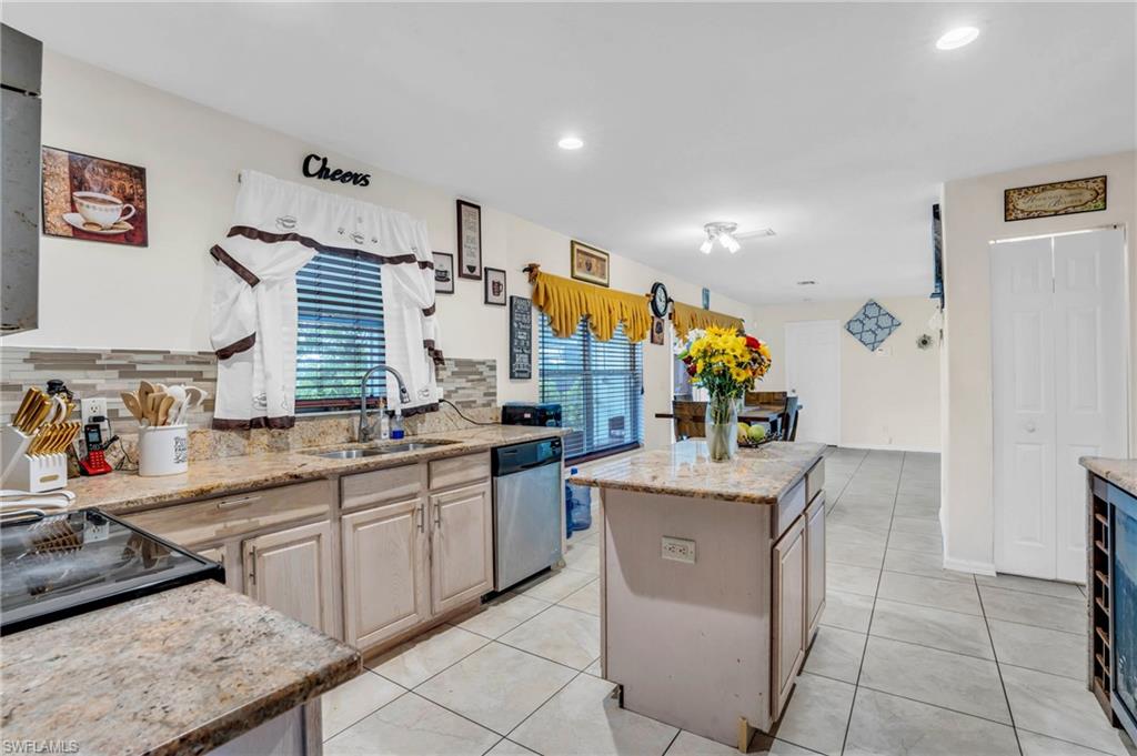 Kitchen featuring decorative backsplash, light brown cabinetry, stainless steel dishwasher, a kitchen island, and sink