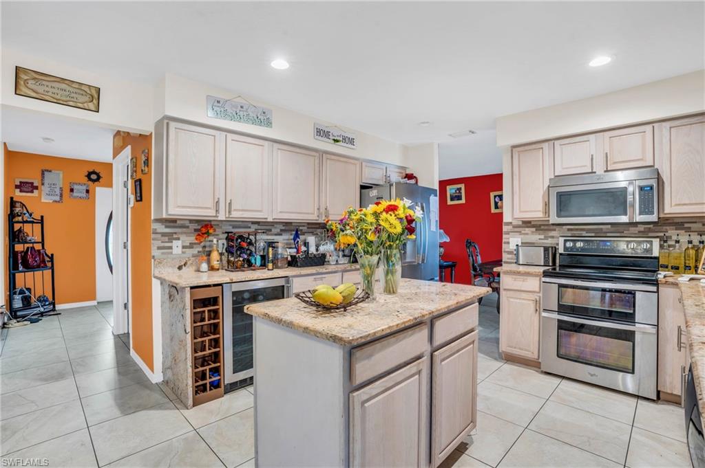 Kitchen with appliances with stainless steel finishes, wine cooler, a kitchen island, and tasteful backsplash