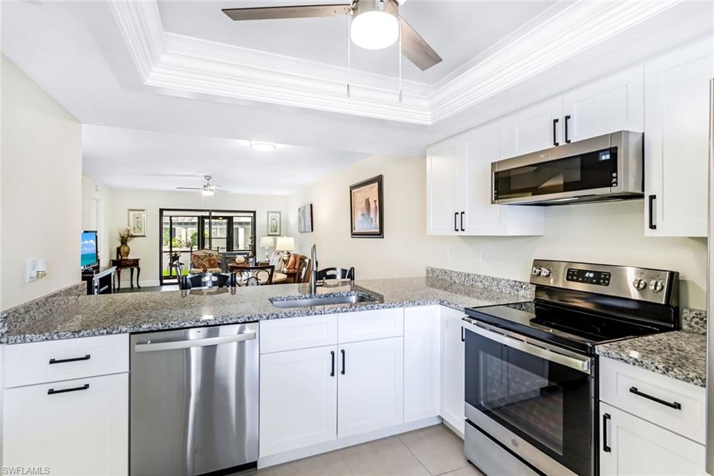 Kitchen with ceiling fan, a tray ceiling, white cabinetry, stone countertops, and appliances with stainless steel finishes