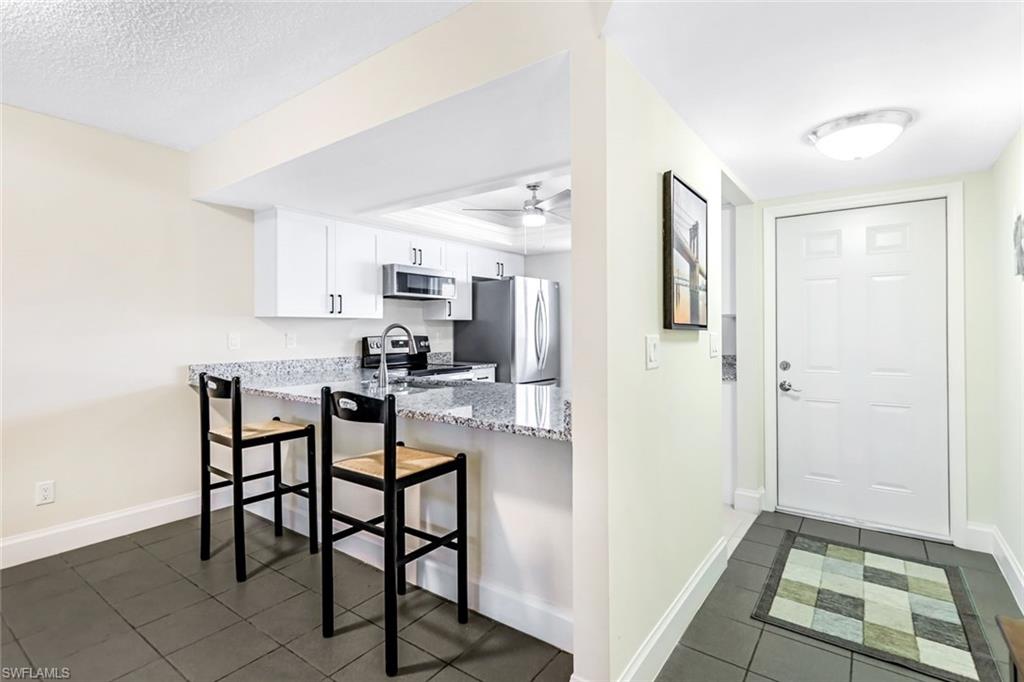 Kitchen with appliances with stainless steel finishes, dark tile patterned floors, light stone countertops, a textured ceiling, and white cabinets