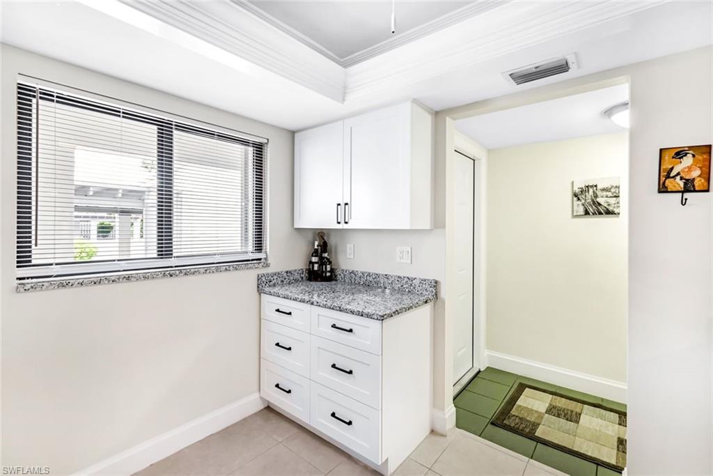Kitchen with light tile patterned floors, ornamental molding, light stone countertops, and white cabinetry