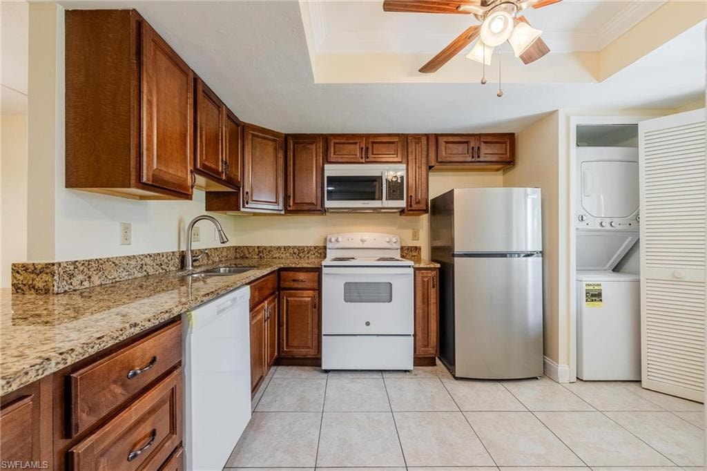Kitchen with granite counters, dark wood cabinets, stacked washer / dryer, crown molding, and a tray ceiling