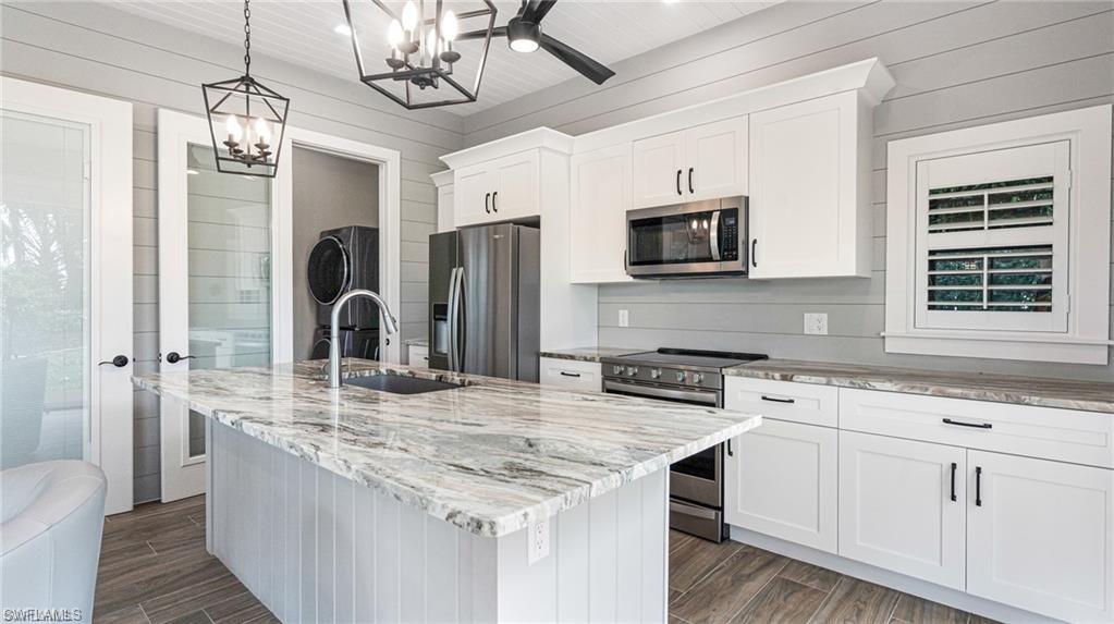 Kitchen, stainless appliances, wood-look flooring, white cabinetry, and a center island with sink