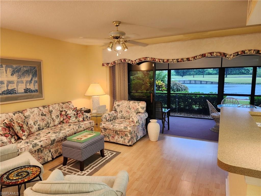 Living room with ceiling fan, a water view, and hardwood / wood-style flooring