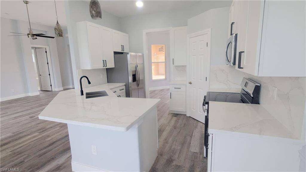 Kitchen with white cabinets, light hardwood / wood-style flooring, appliances with stainless steel finishes, sink, and ceiling fan
