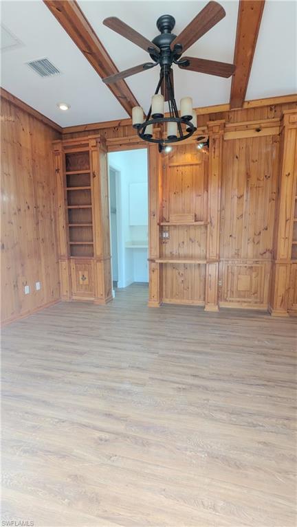 Unfurnished living room featuring light wood-type flooring, ceiling fan with notable chandelier, and wooden walls