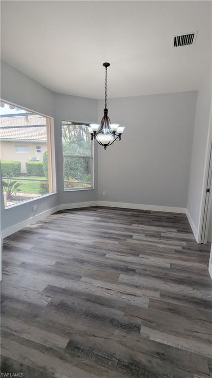 Unfurnished dining area featuring dark wood-type flooring and an inviting chandelier