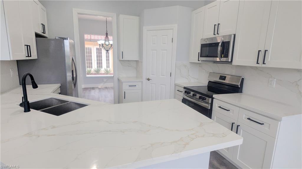 Kitchen featuring appliances with stainless steel finishes, a chandelier, white cabinetry, and sink
