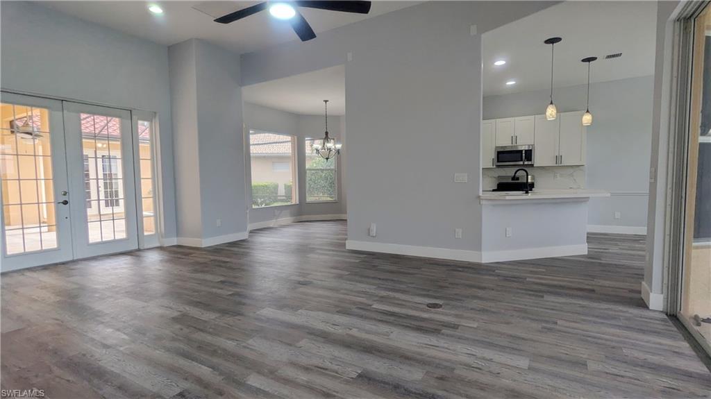 Unfurnished living room with ceiling fan with notable chandelier, french doors, sink, and dark hardwood / wood-style floors