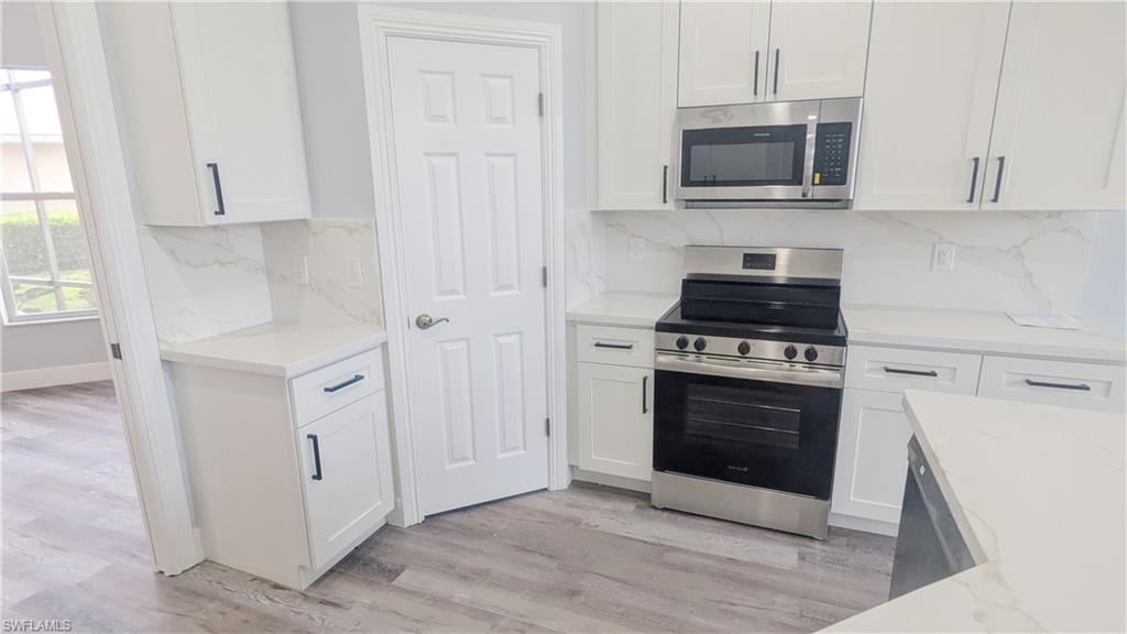 Kitchen featuring stainless steel appliances, light stone countertops, white cabinetry, and light hardwood / wood-style floors