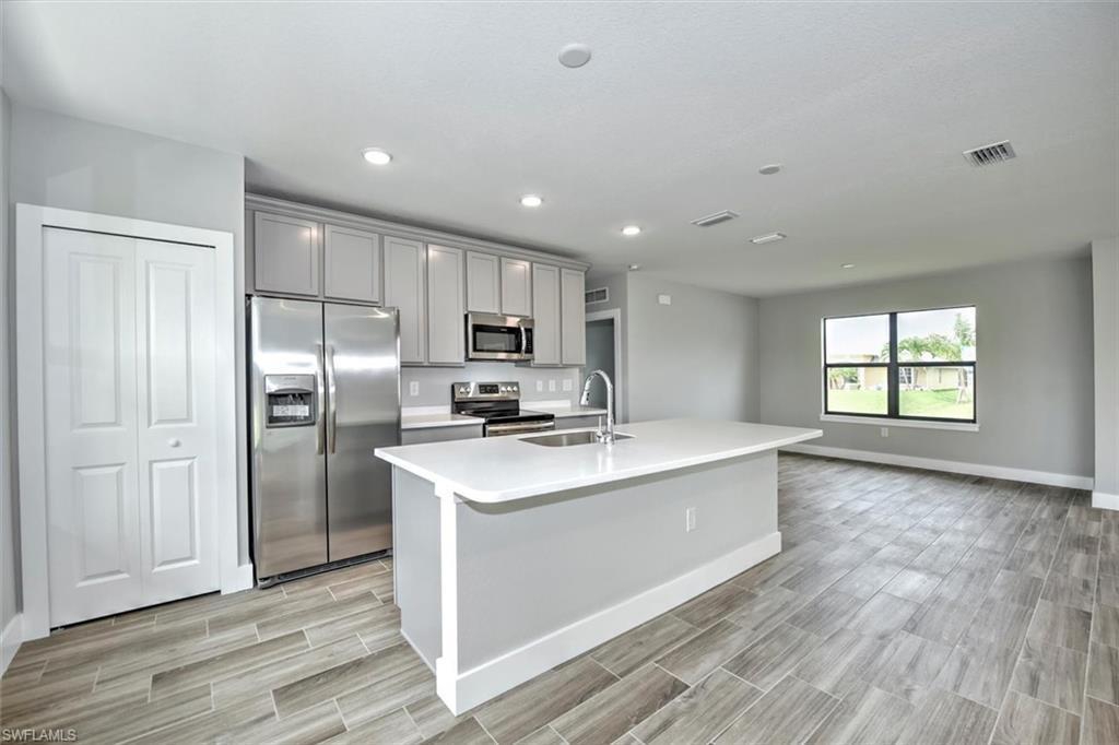 Kitchen with stainless steel appliances, light hardwood / wood-style floors, sink, gray cabinets, and an island with sink