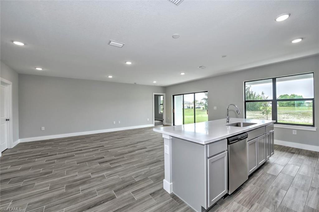 Kitchen with dishwasher, an island with sink, sink, gray cabinets, and light wood-type flooring