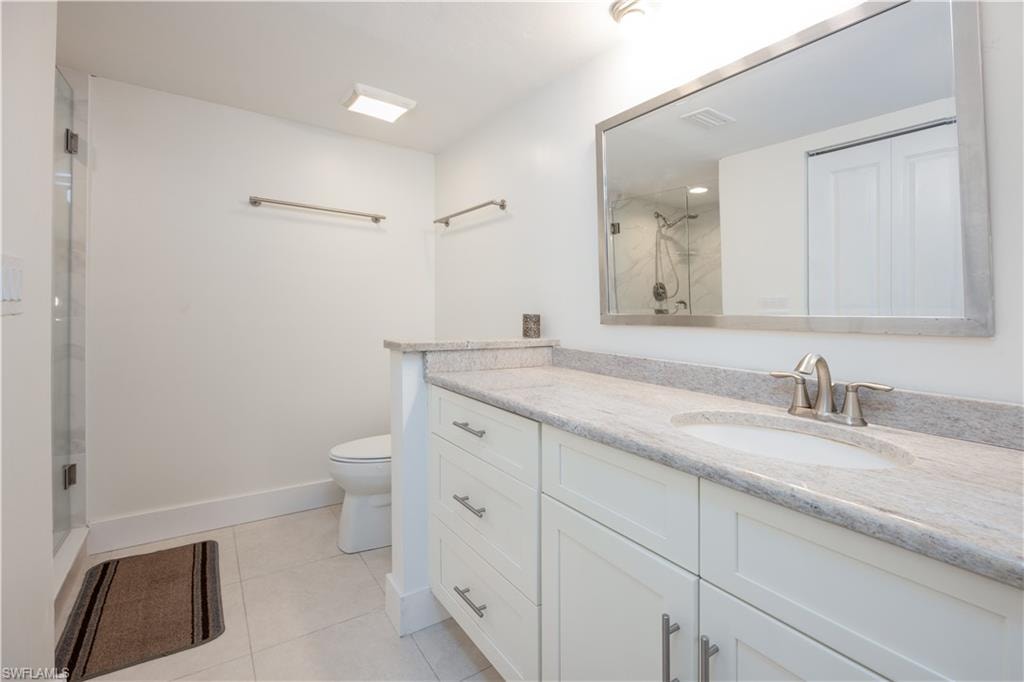 Bathroom with vanity, toilet, an enclosed shower, and tile patterned flooring