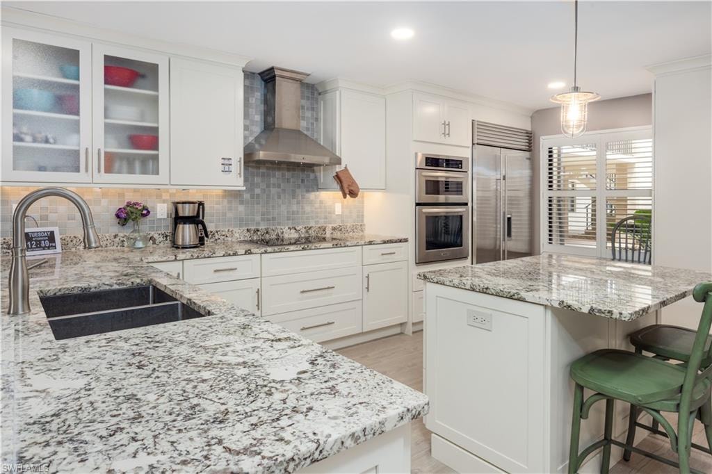 Kitchen with appliances with stainless steel finishes, hanging light fixtures, sink, wall chimney range hood, and white cabinets