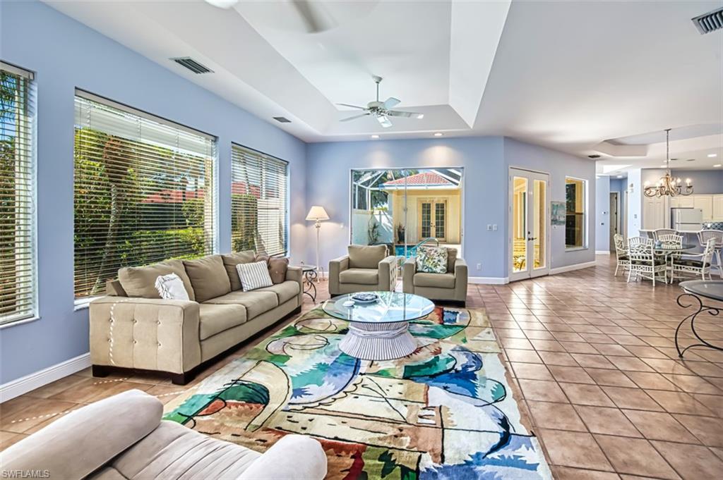 Tiled living room with ceiling fan with notable chandelier and a raised ceiling