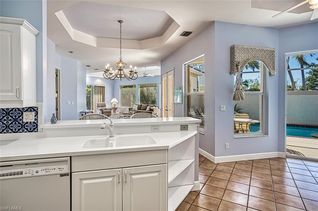 Kitchen with white dishwasher, plenty of natural light, ceiling fan with notable chandelier, and white cabinetry