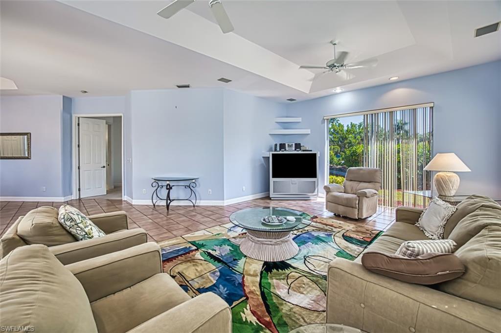 Living room with a tray ceiling, ceiling fan, and light tile patterned flooring