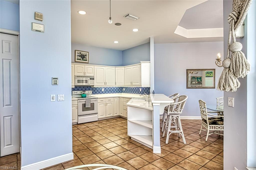 Kitchen featuring white cabinetry, white appliances, kitchen peninsula, a breakfast bar, and light tile patterned flooring