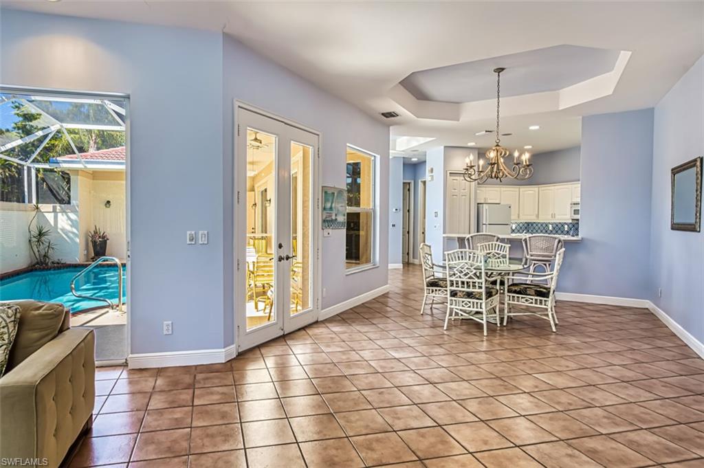 Tiled dining room with a tray ceiling, plenty of natural light, an inviting chandelier, and french doors