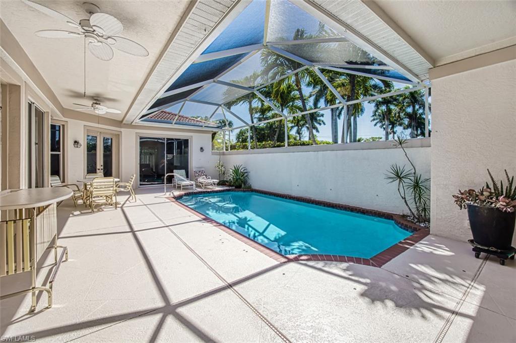 View of pool with glass enclosure, ceiling fan, and a patio