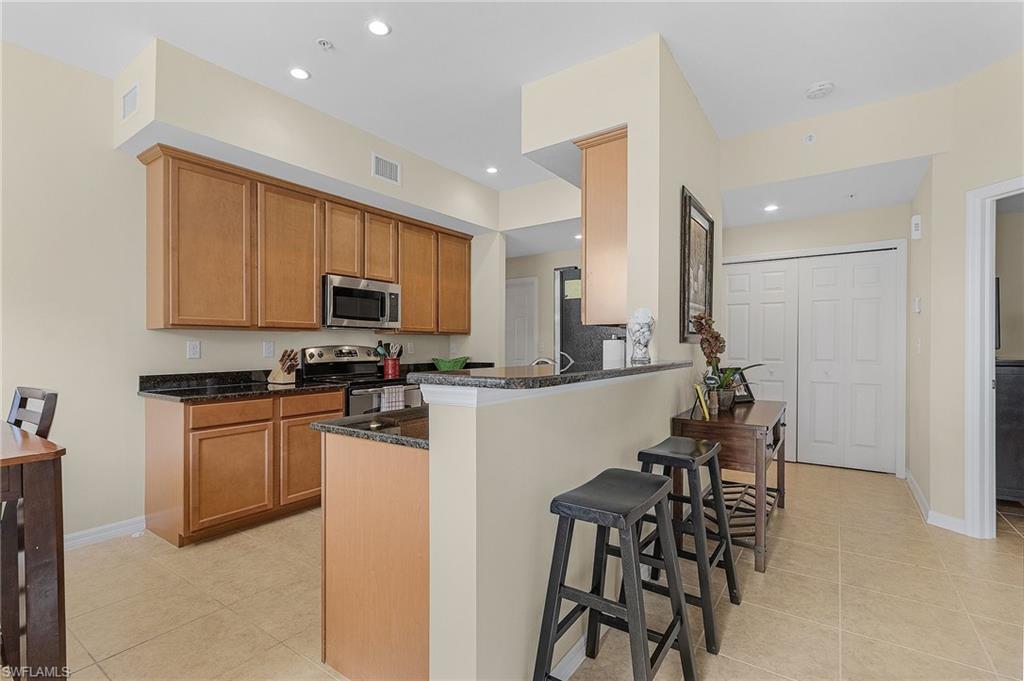 Kitchen with dark stone countertops, light tile patterned floors, stainless steel appliances, kitchen peninsula, and a breakfast bar area