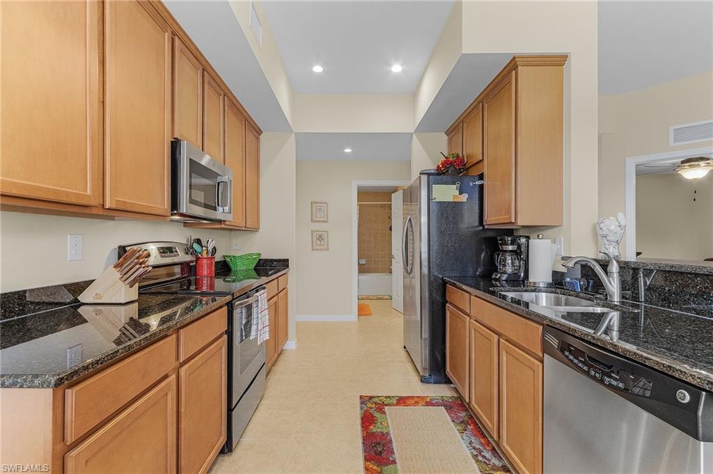 Kitchen featuring dark stone countertops, ceiling fan, stainless steel appliances, and sink