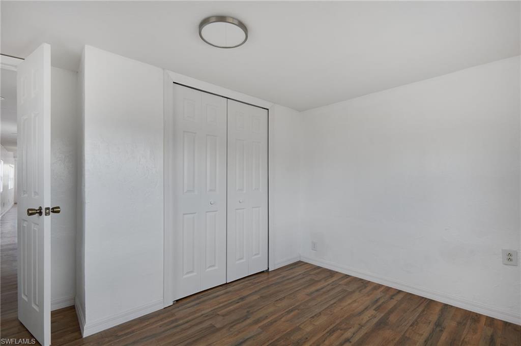 Unfurnished bedroom with baseboards, a closet, and dark wood-style floors