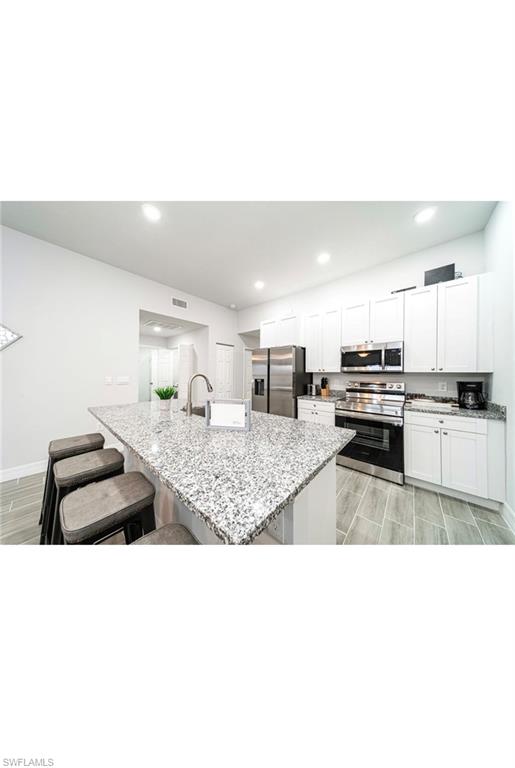 Kitchen featuring appliances with stainless steel finishes, light stone countertops, white cabinetry, a center island with sink, and a breakfast bar