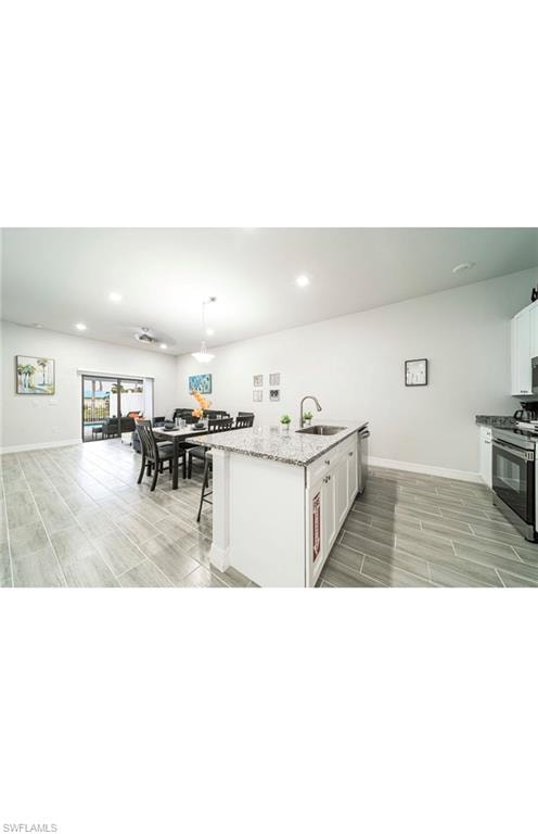 Kitchen featuring white cabinets, appliances with stainless steel finishes, light stone counters, sink, and a center island with sink