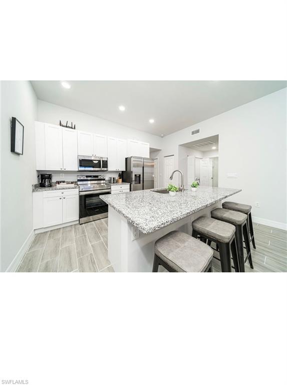 Kitchen with light stone countertops, a kitchen island with sink, a kitchen bar, stainless steel appliances, and white cabinets