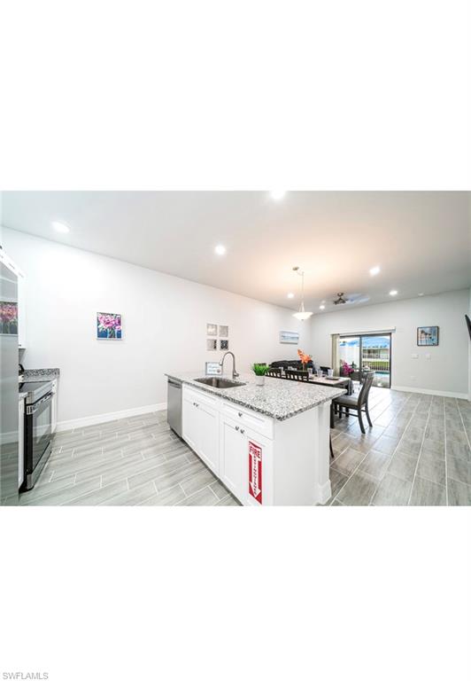 Kitchen with white cabinets, decorative light fixtures, appliances with stainless steel finishes, sink, and a center island with sink