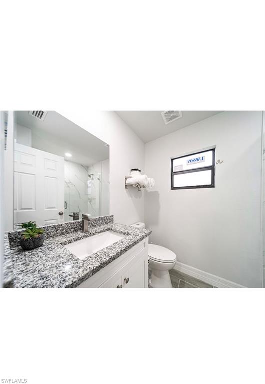Bathroom with a shower with door, vanity, toilet, and tile patterned floors