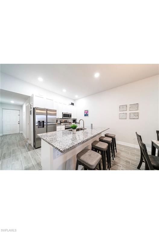 Kitchen with a breakfast bar area, light stone countertops, light hardwood / wood-style flooring, appliances with stainless steel finishes, and white cabinetry