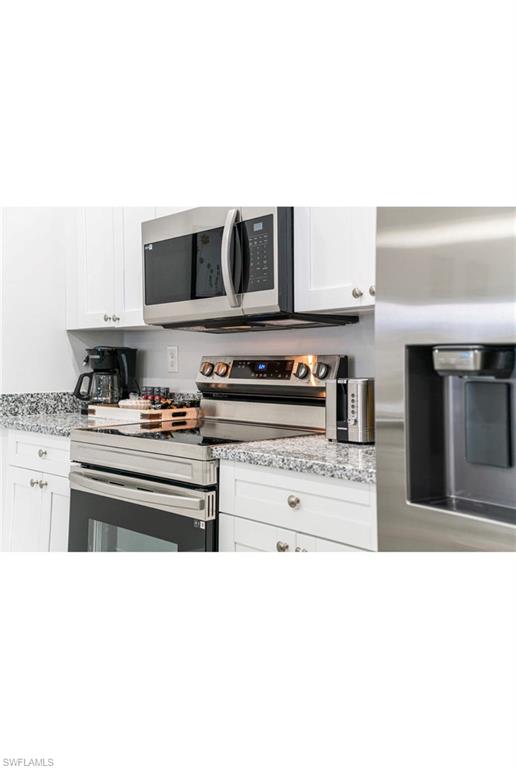 Kitchen with light stone counters, appliances with stainless steel finishes, and white cabinetry