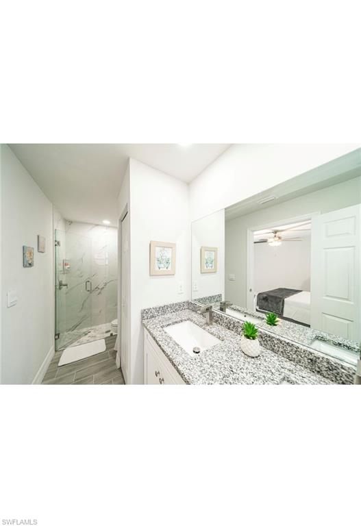 Bathroom featuring vanity, hardwood / wood-style flooring, walk in shower, and ceiling fan