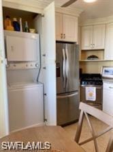 Kitchen featuring stacked washer and clothes dryer, stainless steel refrigerator with ice dispenser, and stove