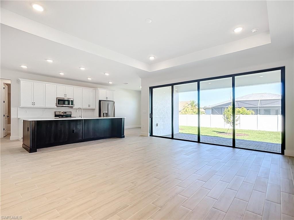 Kitchen featuring white cabinets, an island with sink, sink, stainless steel appliances, and light hardwood / wood-style floors