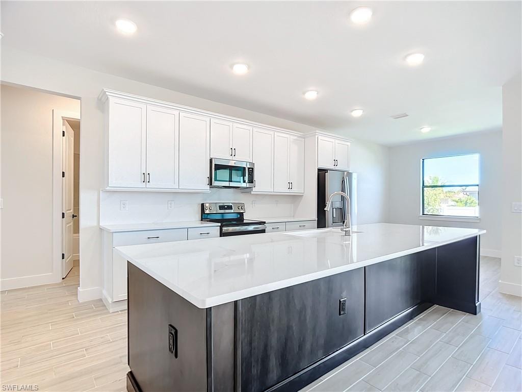Kitchen featuring white cabinets, light wood-type flooring, appliances with stainless steel finishes, and a large island with sink