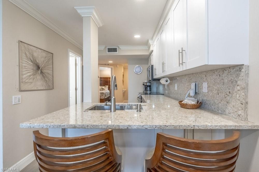 Kitchen featuring a breakfast bar, sink, white cabinets, crown molding, and light stone countertops