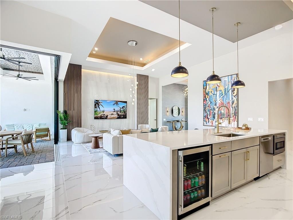 Kitchen with a raised ceiling, beverage cooler, ceiling fan, decorative light fixtures, and sink