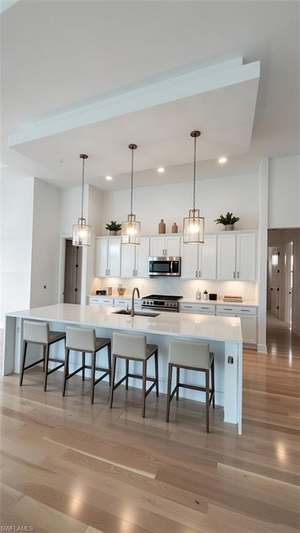 Kitchen with a large island with sink, a breakfast bar, white cabinets, pendant lighting, and light wood-style floors