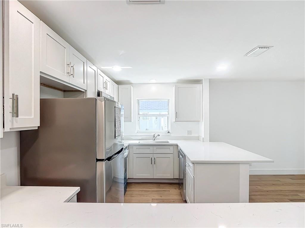 Kitchen featuring stainless steel appliances, white cabinets, kitchen peninsula, and light hardwood / wood-style floors