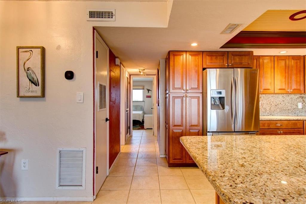 Kitchen featuring light stone countertops, tasteful backsplash, light tile patterned flooring, and stainless steel fridge